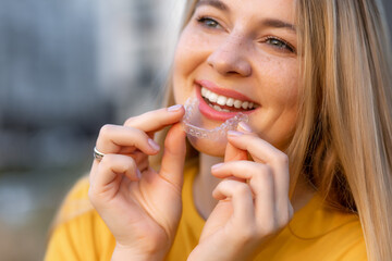 Smiling woman holding a clear dental aligner outdoors in natural light