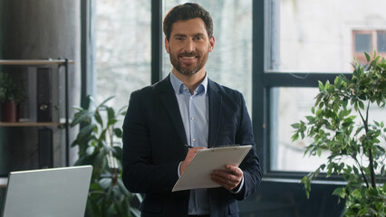 Focused adult caucasian man recruiting agent standing in office making notes writing checklist businessman conducts inspection write strategic plan showing thumb up gesture approval best choice sign