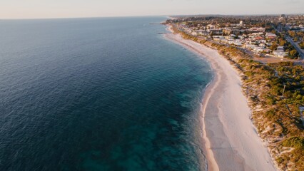 Aerial view captures tranquil ocean coastline with peaceful beach and residential buildings. Clear skies enhance the serene atmosphere.