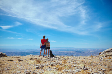 Couple Admiring Scenic Mountain View Under Clear Blue Sky with Pet