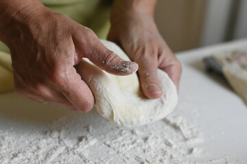 Hands holding dough over a table sprinkled with flour, process of making homemade pastry.