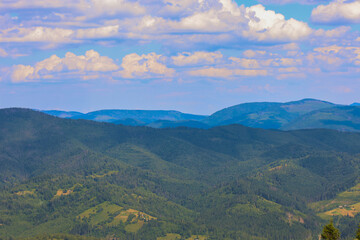 Obraz premium ​A rolling mountain range, covered with emerald-green forests, creates an impressive panoramic view that conveys peace and tranquility.