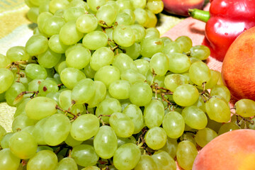 Ripe and juicy fruits such as green and blue grapes, peaches and persimmons lie on the table.