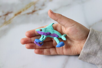A plasticine figure made by a child in the shape of a shark in children's hands, close-up.