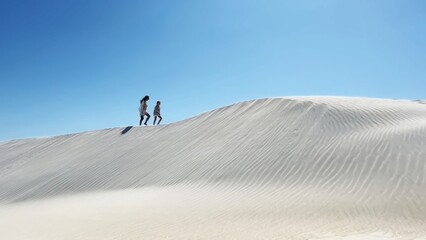 Woman and girl walk peacefully across sandy desert dunes. Daytime scene evokes serenity and quiet connection in nature.