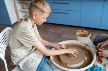 Boy sculpting clay on pottery wheel, children's activity with teacher