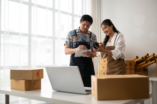 Two online sellers managing orders in warehouse using laptop and smartphone