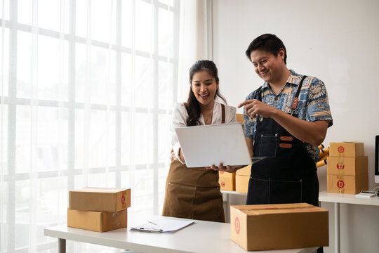 Two happy sme business owners checking online orders on laptop in warehouse