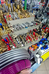 Assortment of plumbing supplies in hardware store, including fittings, valves, pipes, connectors, hoses, and tools. Various metal and plastic components organized on display shelves.