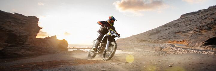 Creative collage with focused biker rides through desert canyon with rocks and glowing sun in background. Extreme sport adventures. Concept of motorsport, speed, travel. 3D render of background. © master1305