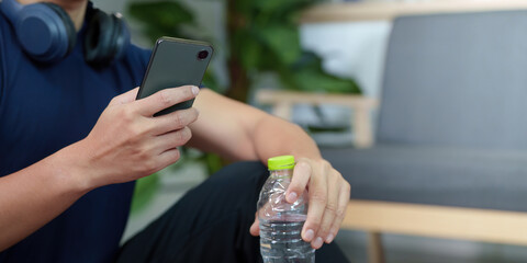 Hydration and Technology. Young man using smartphone while holding a water bottle.