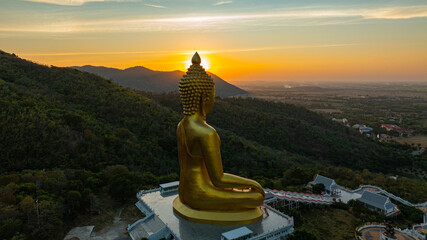 An awe-inspiring view of a big golden Buddha statue atop a hill overlooking a serene valley,...