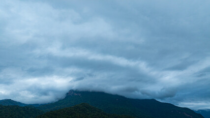 A dramatic view of a lush, forested mountain peak shrouded in thick clouds, capturing the raw beauty and mystique of nature under an overcast sky.