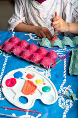 Child painting an egg box with a brush