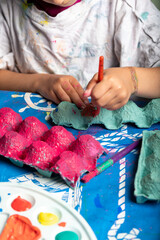 Child painting an egg box with a brush