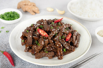 Teriyaki beef stir-fry with sesame seeds and chili pepper on a white plate. Asian cuisine. Top view.