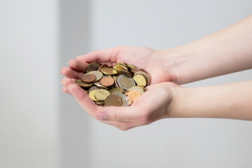 Folded hands holding or extending a stack of coins. Petty cash, handout, tip, last savings, financial donations. Value of coin savings