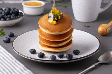 A stack of pancakes is drizzled with honey. Blueberries are placed next to the pancakes