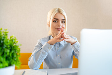 Confident businesswoman with clasped hands at desk during remote meeting or online interview in modern home office for digital career, leadership, consulting, professional growth, coaching.