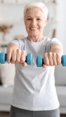 Home training concept. Strong senior woman doing exercises with dumbbells indoors. Cheerful mature lady working out her arm muscles, keeping fit, leading healthy lifestyle during covid-19 isolation