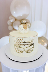 White cake with angel and inscription “Sacrament of Baptism”, decorated with wings and golden details.
