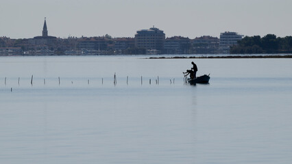 Two fishermen in a small boat work on a fish trap system in the Grado Lagoon. Grado, Friuli Venezia Giulia, Italy.
