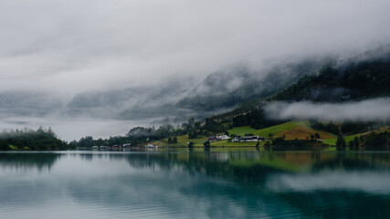 A serene view of Bergheimsvatnet in Norway, where calm waters mirror mist-covered mountains.