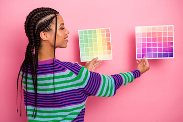 Pretty woman holding two colorful palettes against a pink background, wearing a striped pullover...