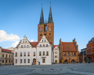 An idyllic historic town square with a monumental church, a town hall, and people outside a café...