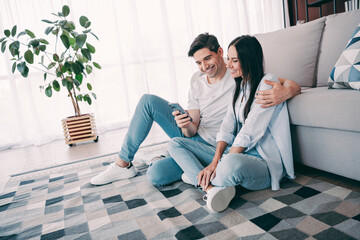 Young couple enjoying leisure time together on the living room floor, bonding over shared moments with a smartphone in hand