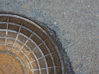 A close-up of a rusty cast-iron manhole cover and an asphalt road in the background.