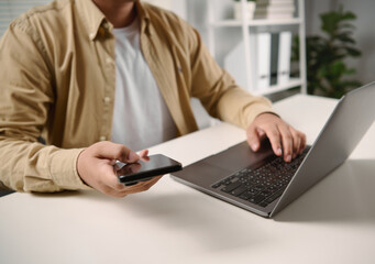Man using smartphone with laptop on desk for mobile communication online business management remote work digital productivity internet connection and modern workplace technology