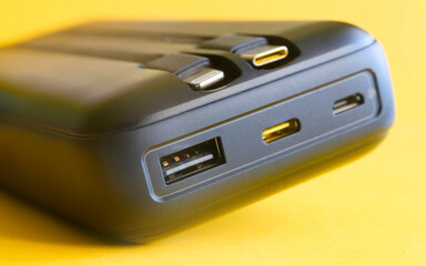 Fototapeta premium High‑capacity power bank on yellow with built‑in USB‑C and Lightning leads plus USB‑C, micro‑USB and USB‑A ports; fast charge hub for phones and tech on the go. Photo