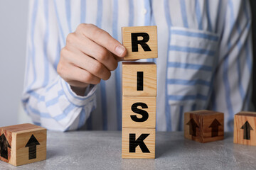 Woman putting wooden cube with letter R to make word Risk at table, closeup