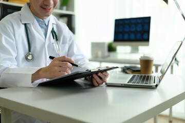 Close-up of a medical professional reviewing a patient chart and enters information into a laptop during a focused work session