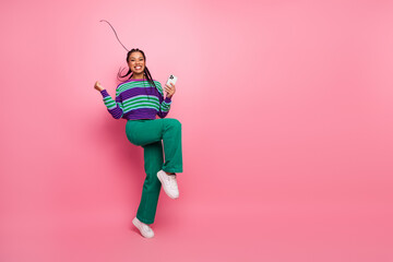 Joyful young woman with striped sweater holding smartphone and cheering on vibrant pink background