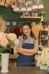 Asian female florist in apron smiling while designing a beautiful floral arrangement with her colleague in a flower shop. Concept of teamwork, creativity, floral business, and joyful workplace.