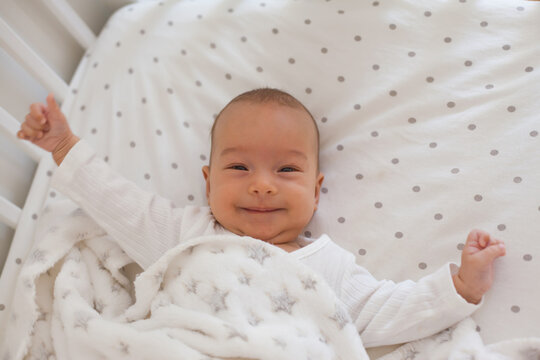 Smiling baby on white bedding with soft fleece blanket