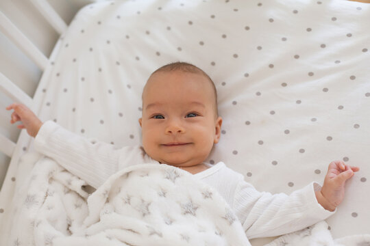 Smiling baby on white bedding with soft fleece blanket