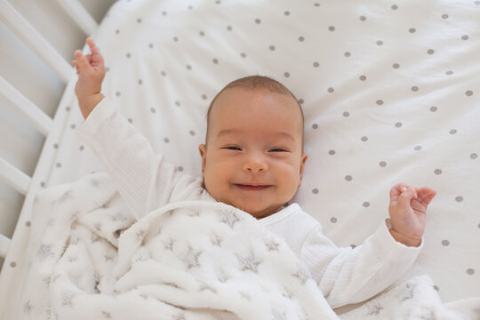 Smiling baby on white bedding with soft fleece blanket