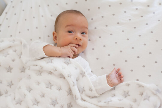 Smiling baby on white bedding with soft fleece blanket