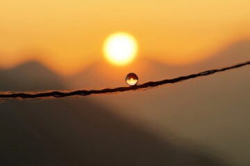 A stunning sunrise reflecting in a water droplet on a wire, with mountains fading in the background, creating a serene atmosphere.