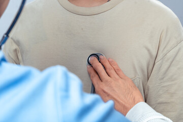 Close-up of an Asian person using a stethoscope on chest for medical check-up, symbolizing health monitoring, diagnosis, and healthcare examination on plain background