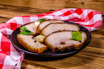 Slices of baked pork belly, garlic and parsley on a black plate