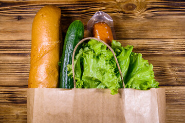 Paper bag with different food from grocery on a wooden table. Supermarket shopping concept. Top view
