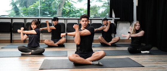 Diverse sporty men and women doing stretching exercises during group yoga lesson