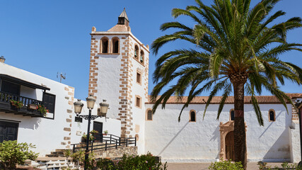 Historic church in Betancuria, Fuerteventura. A palm tree, whitewashed walls, and colonial architecture under a bright blue sky in this traditional Canarian village.
