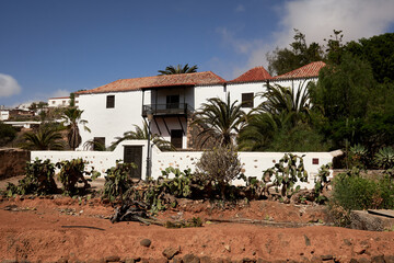 Traditional house in Betancuria, Fuerteventura, with whitewashed walls, red-tiled roof, palm trees, and rustic charm under a bright blue sky.
