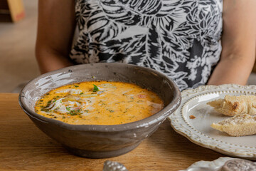 A person at the table eating creamy soup served with bread in a casual dining setting