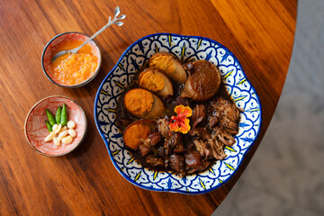 Thai braised pork belly with eggs (Kai Pa-Lo) served in traditional patterned bowl with condiments.